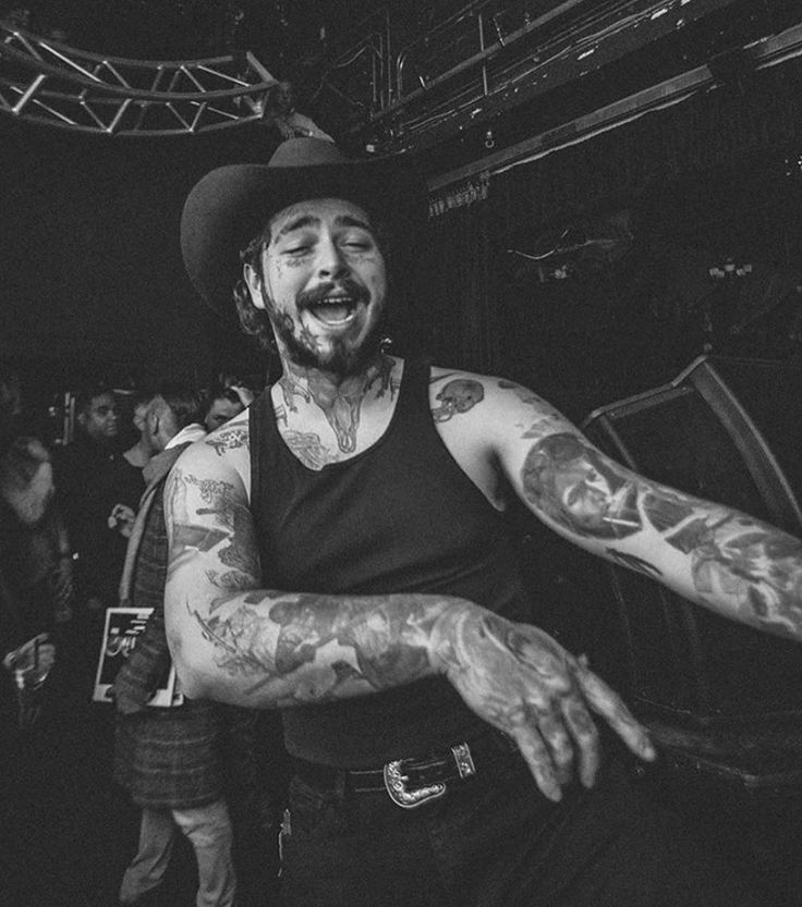 black and white photograph of a man with tattoos on his arms, wearing a hat