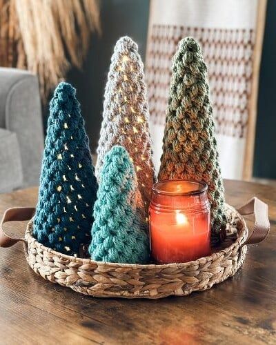 small crocheted trees sitting on top of a table next to a lit candle