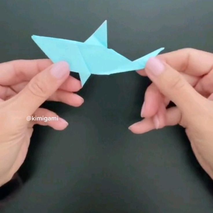 two hands holding an origami fish in one hand and another hand reaching for it