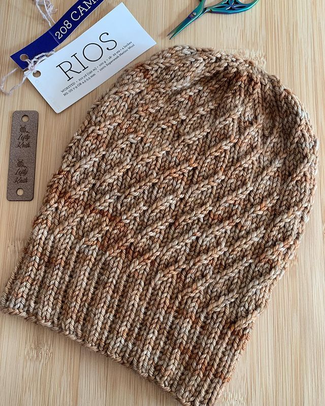 a knitted hat sitting on top of a wooden table next to eyeglasses