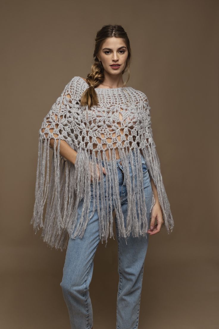 a woman standing in front of a brown background wearing a white crochet shawl