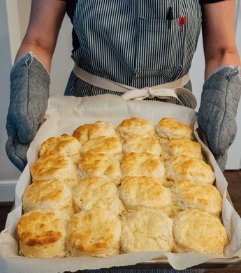 a person in an apron holding a tray of biscuits