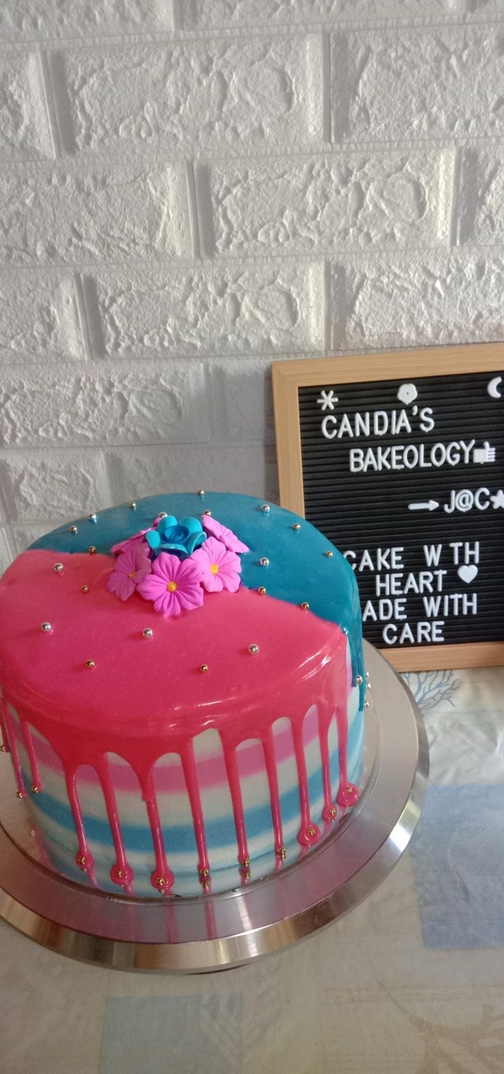 a pink and blue cake sitting on top of a table next to a chalkboard