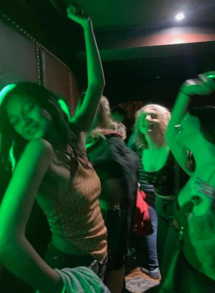 a group of young people dancing in a dark room with green light on the walls