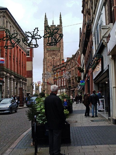 an old man is standing on the sidewalk in front of a building with a clock tower