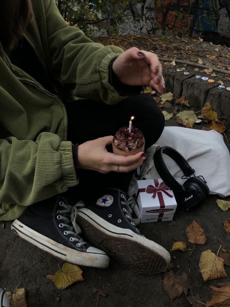 a woman sitting on the ground holding a small cake with a candle in her hand