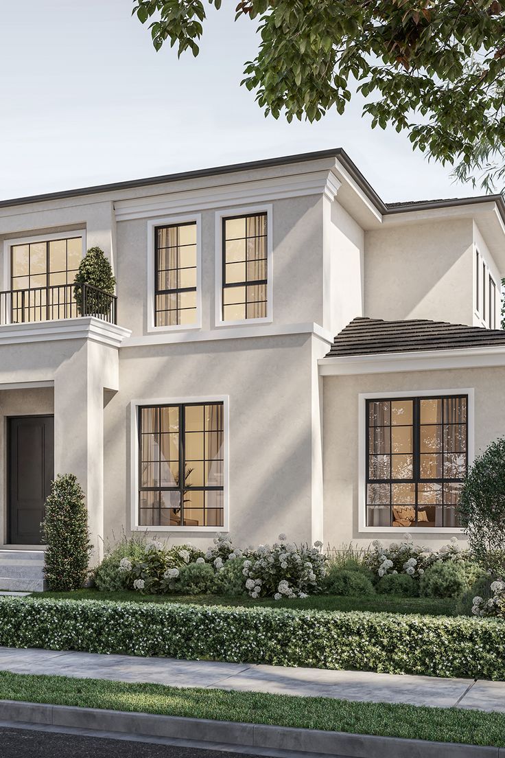 a white two story house with lots of windows and plants on the front lawn area