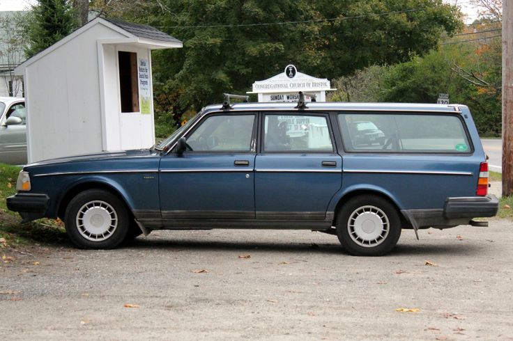 an old blue station wagon parked in front of a small white building with a radio on top