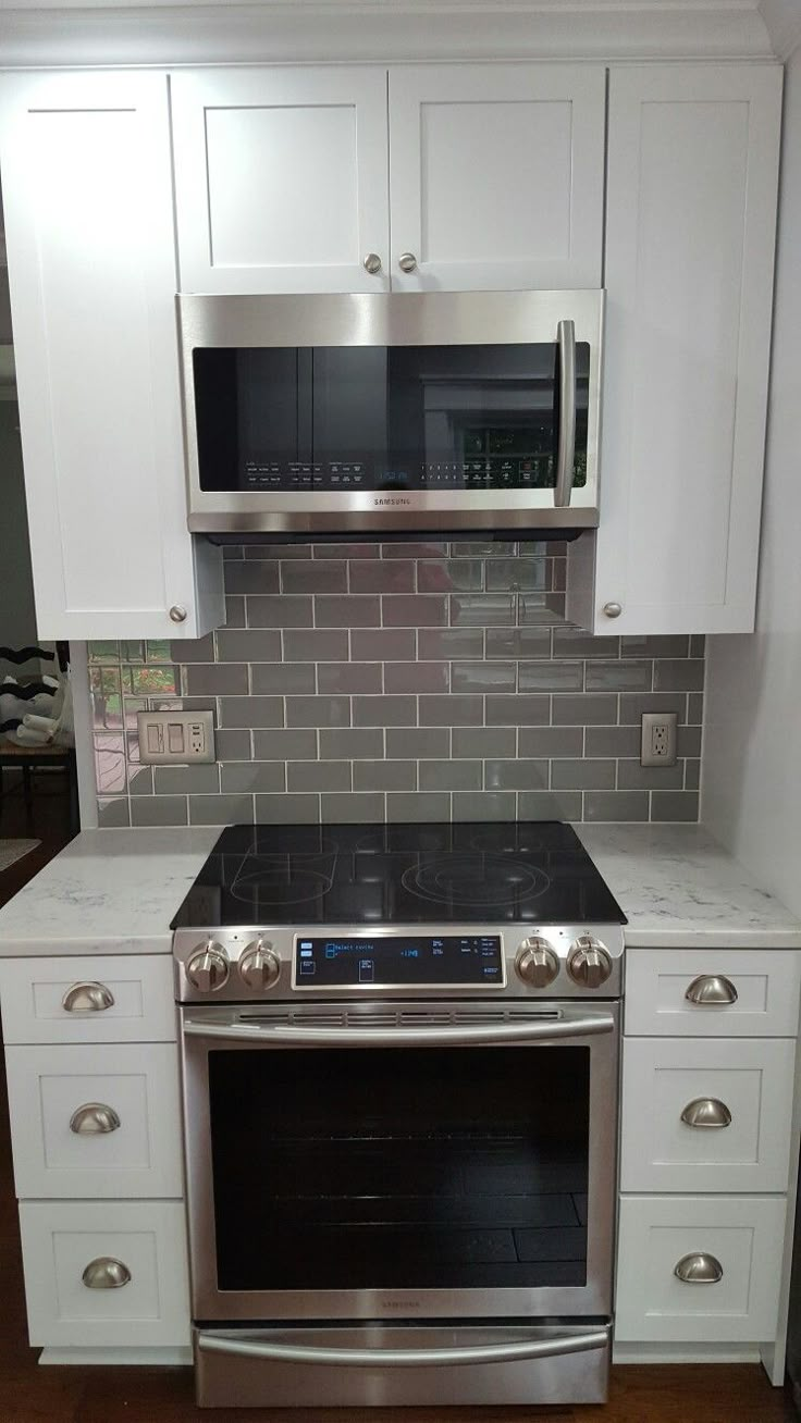 a kitchen with white cabinets and stainless steel stove top oven in the middle of it