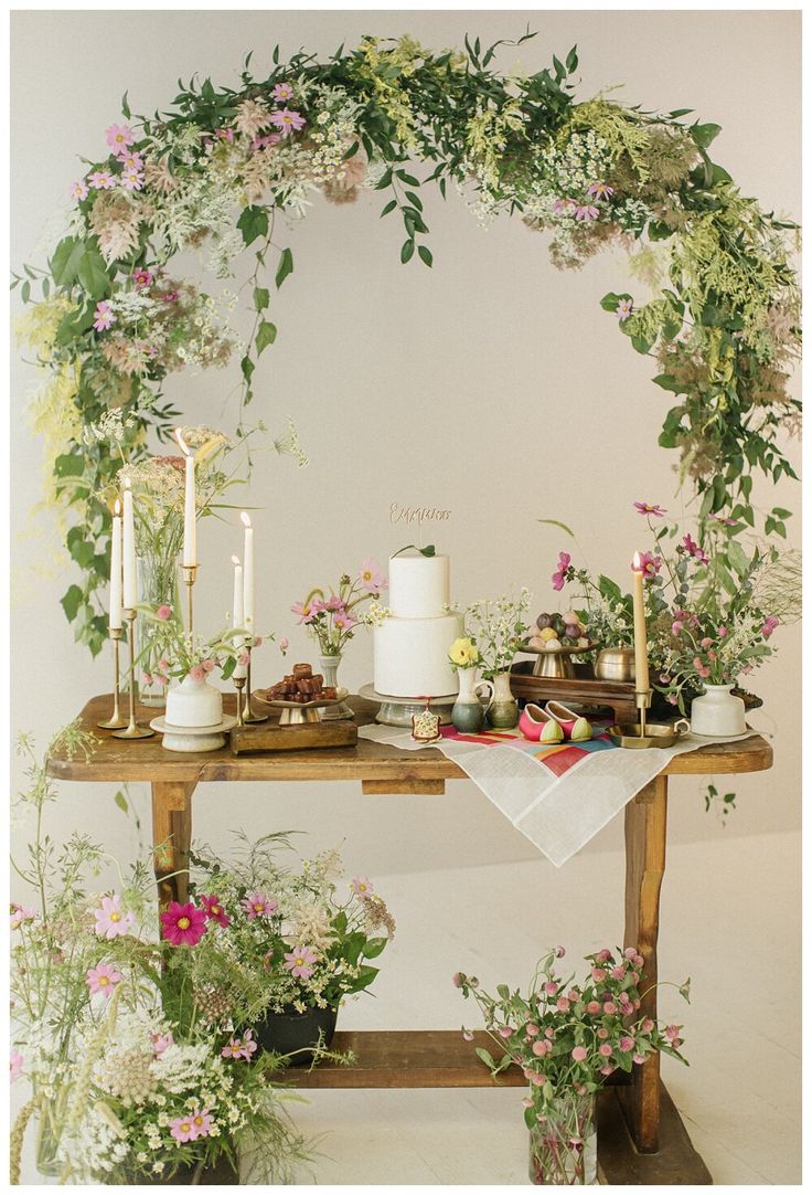 a table topped with lots of flowers and candles next to a wall covered in greenery