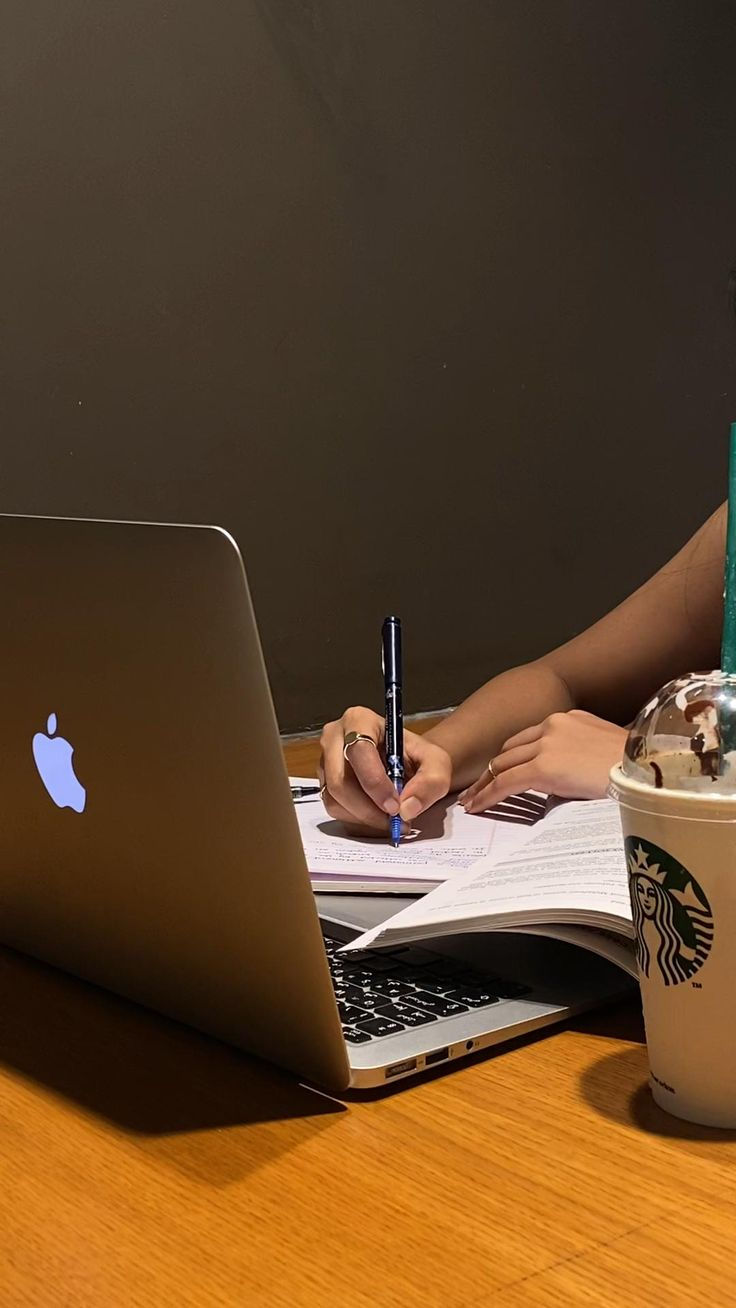 a woman sitting at a table working on her laptop and holding a pen in one hand