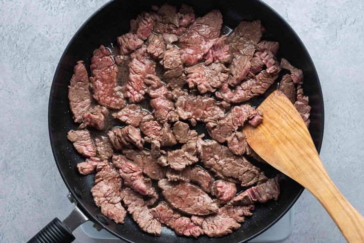 steak being cooked in a skillet with a wooden spoon