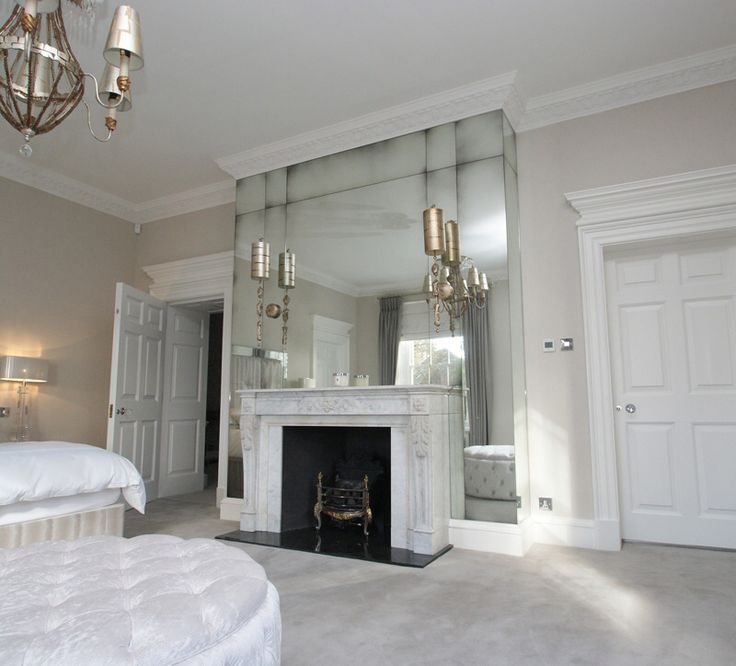 a bedroom with a fireplace and mirror in the corner, next to a white bed