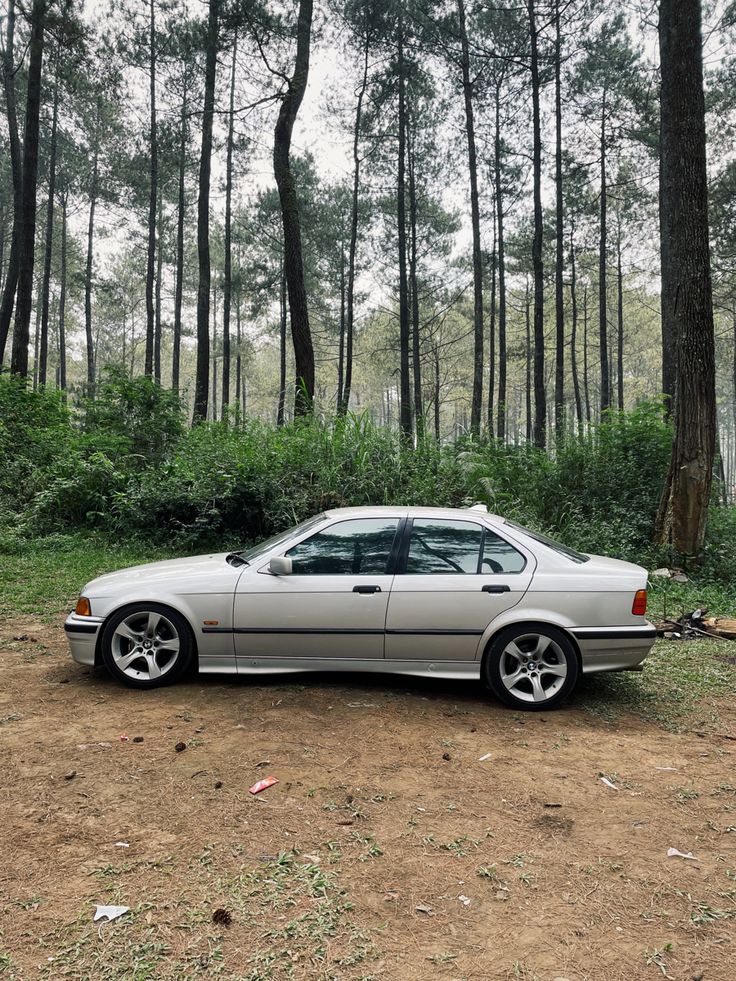 a silver car parked in the middle of a dirt field next to some tall trees