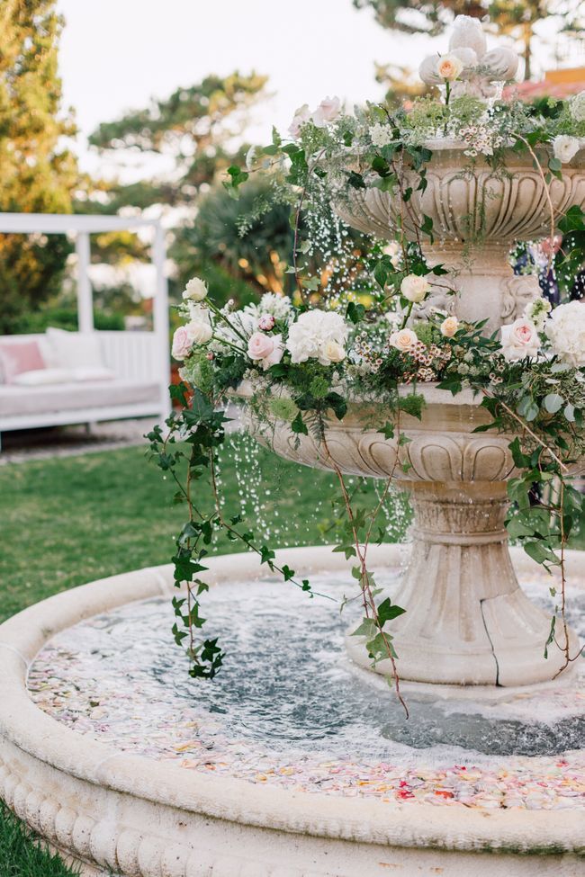 a fountain with flowers and greenery on it in the middle of a lawn area