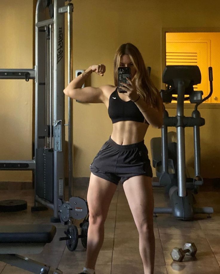 a woman taking a selfie in front of a gym machine with her cell phone