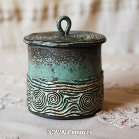 a green and black pot sitting on top of a white tablecloth covered floor next to a lace doily