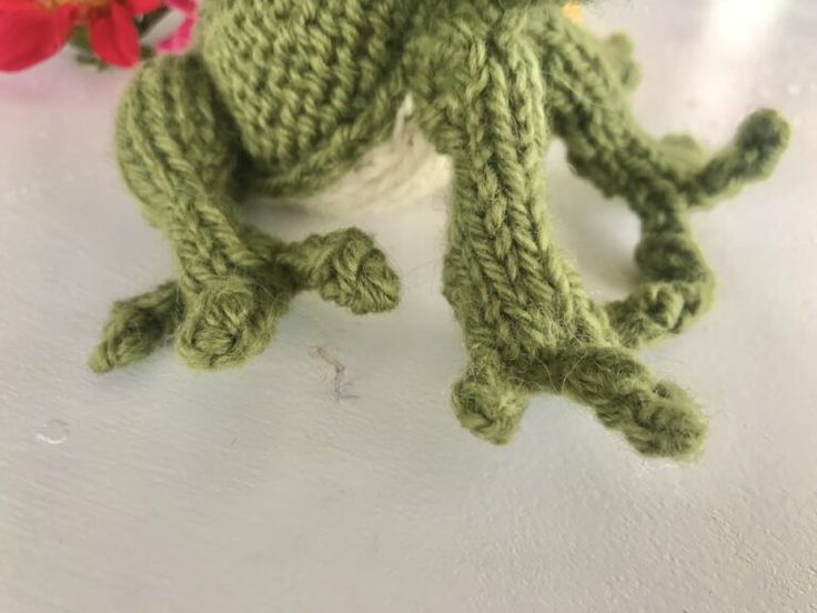 a knitted frog sitting next to a flower