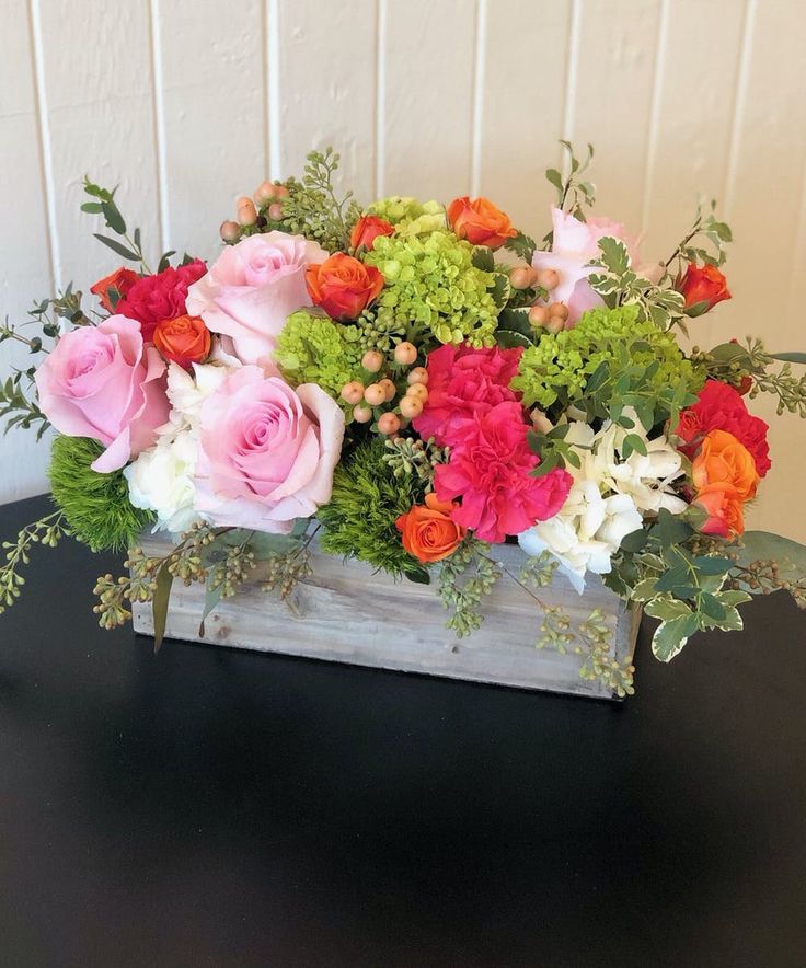 a wooden box filled with lots of flowers on top of a black table next to a white wall