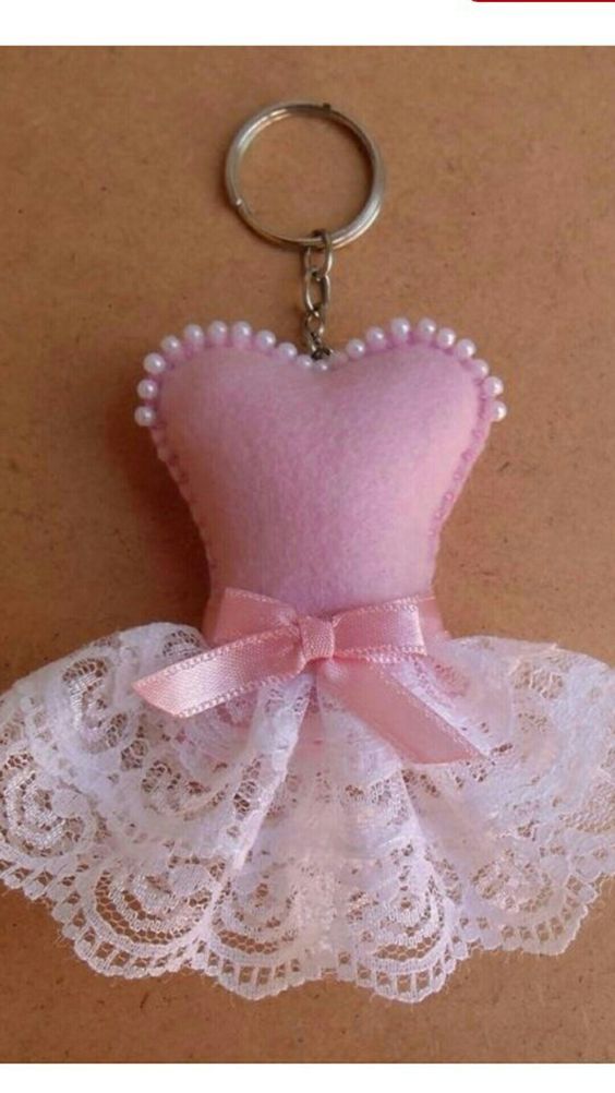 a pink and white dress keychain is hanging on a brown surface with lace