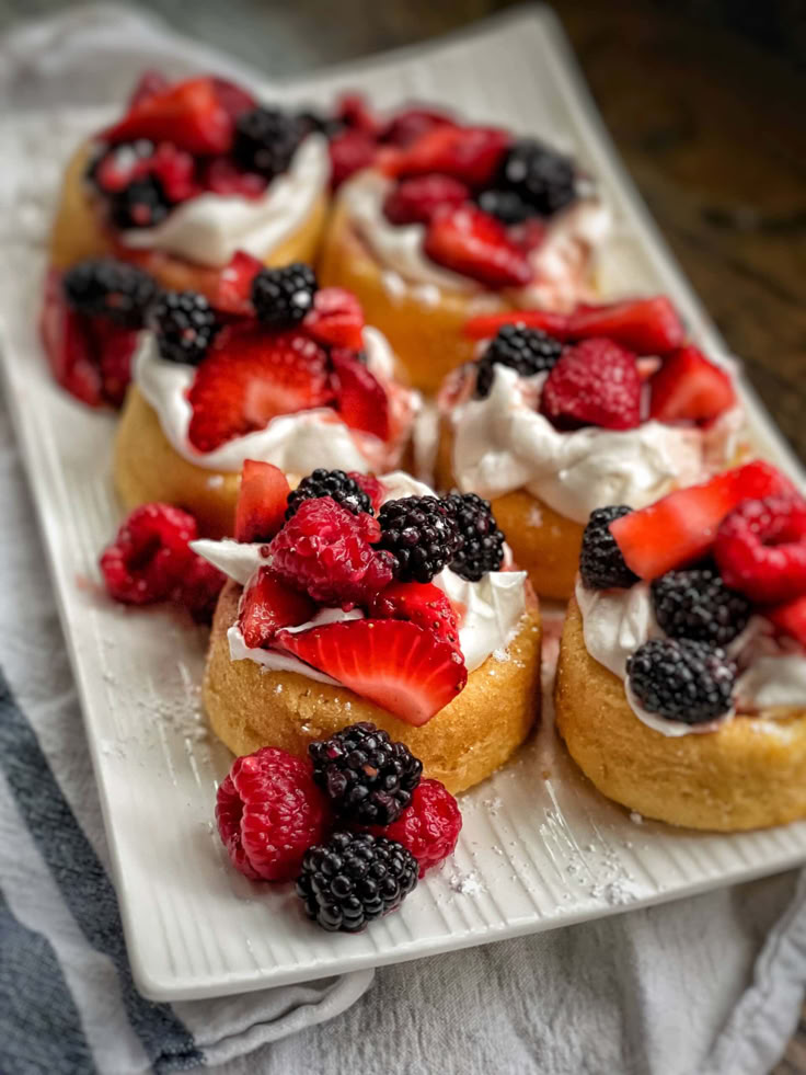 small pastries with berries and whipped cream on a white plate next to a striped towel