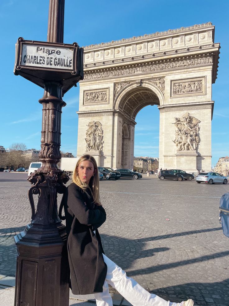 a woman leaning against a lamp post in front of the arc de trioe