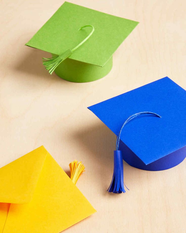 an origami graduation cap and tassel on top of a wooden table next to colored envelopes