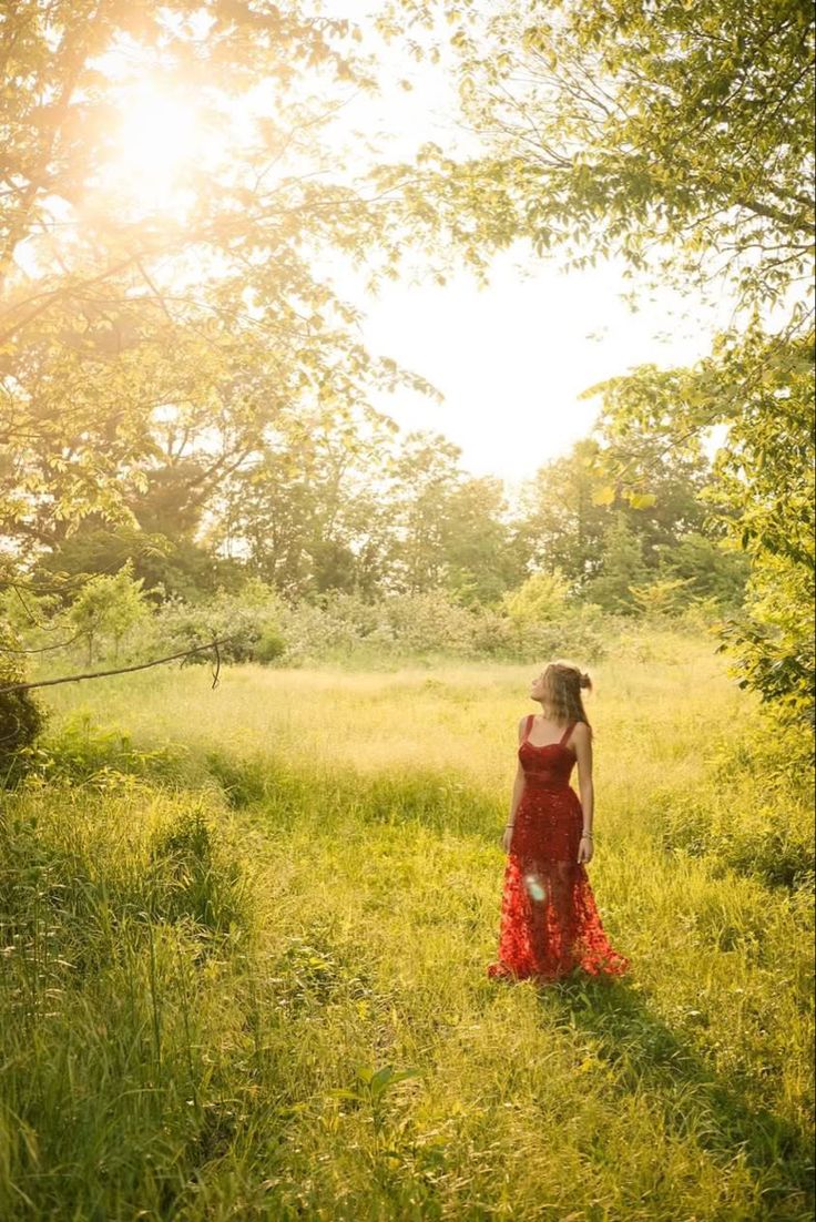 a woman in a red dress is standing in the grass and looking up into the sky