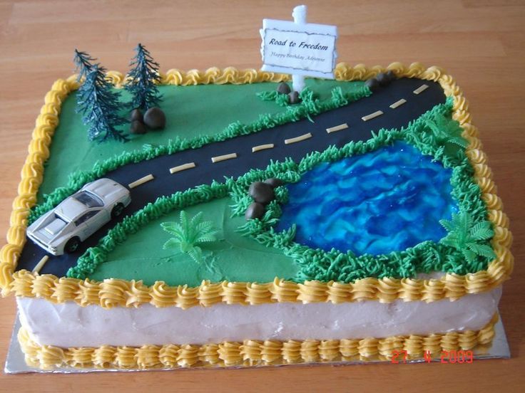 a cake that is shaped like a road with a lake and cars on it, sitting on top of a wooden table