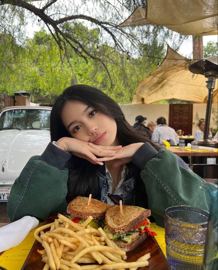 a woman sitting at a table with a sandwich and french fries in front of her