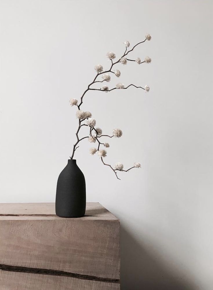 a black vase sitting on top of a wooden table next to a white wall with flowers in it