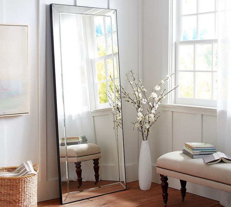 a large mirror sitting on top of a wooden floor next to a vase filled with flowers