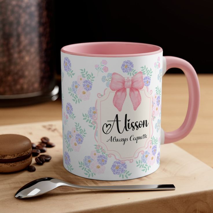 a pink and white coffee mug sitting on top of a wooden table next to a cookie