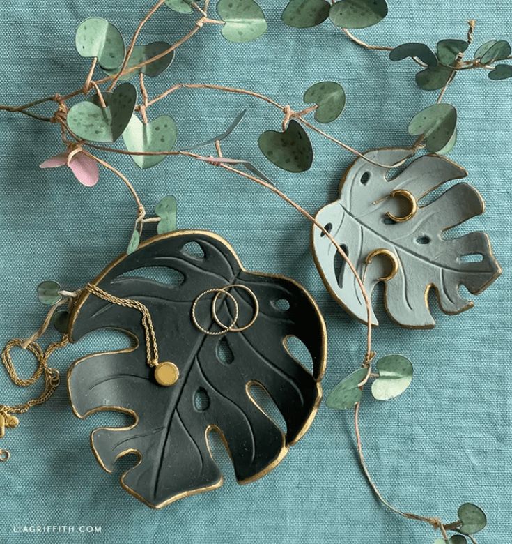 two leaf shaped pendants sitting on top of a blue cloth covered table next to green leaves