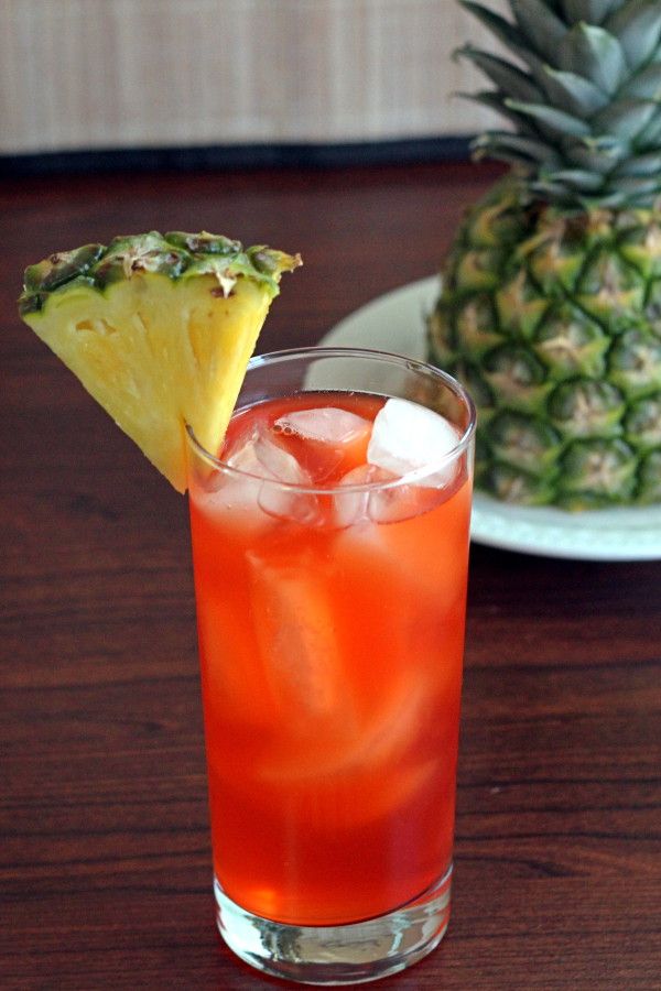 a pineapple drink in a tall glass on a table next to a plate with a pineapple