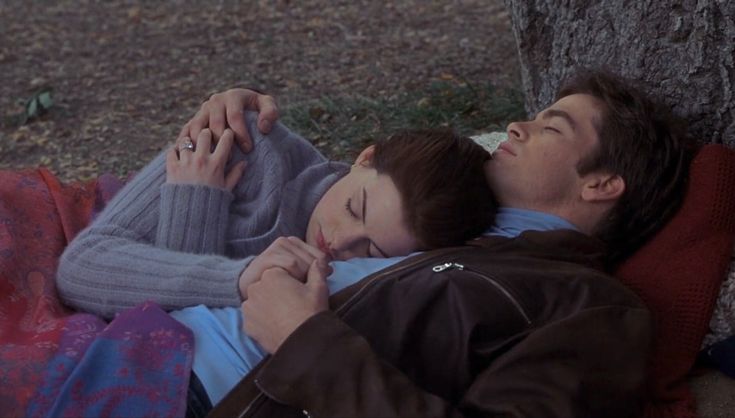 a man and woman laying next to each other under a tree