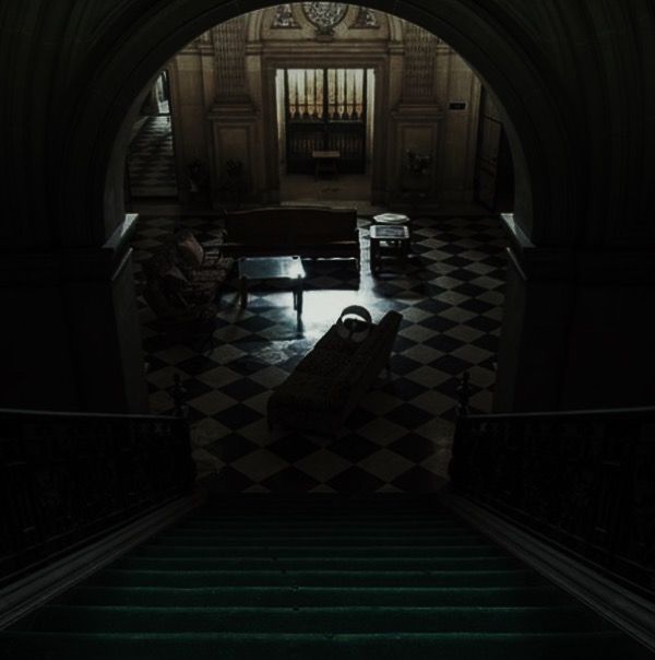 a dark hallway with stairs leading up to a clock on the wall and a black and white checkered floor