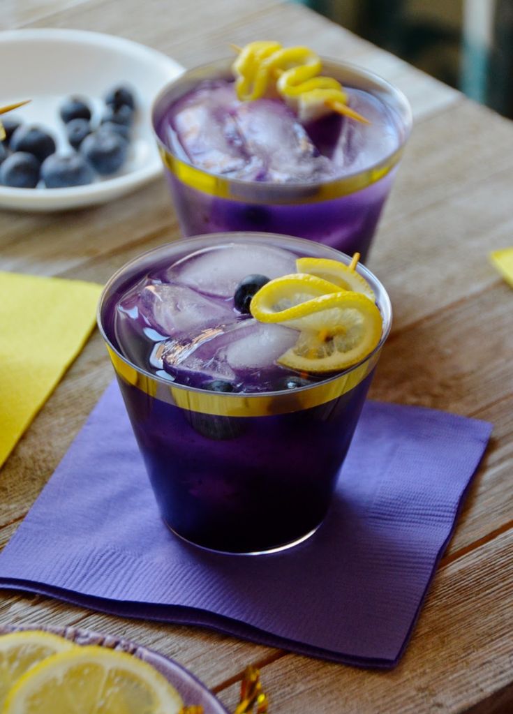 two glasses filled with blueberry lemonade on top of a wooden table