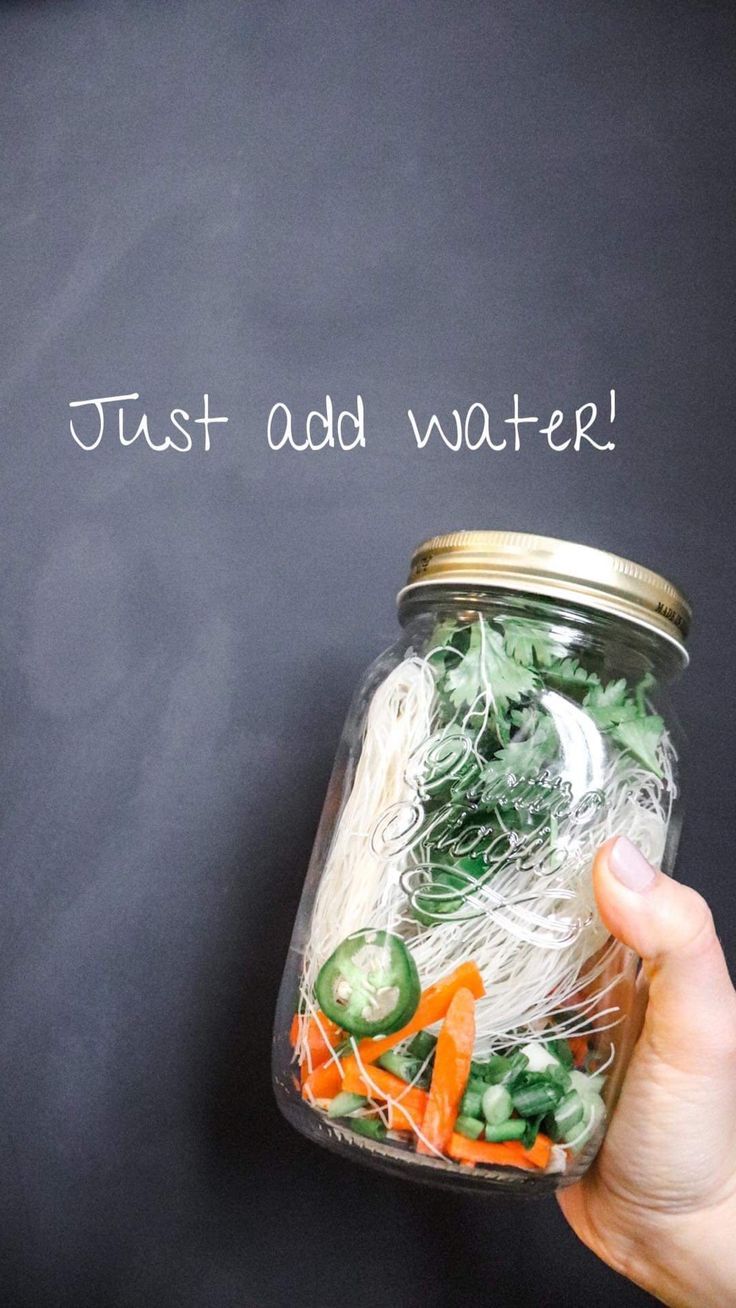 a hand holding a jar filled with pasta and veggies that says just add water