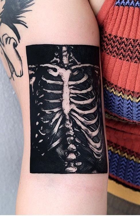 a person with a tattoo on their arm holding up a piece of paper that looks like a skeleton