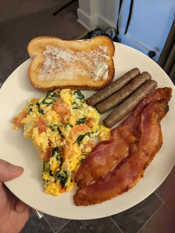 a white plate topped with eggs, sausages and bacon on top of toasted bread