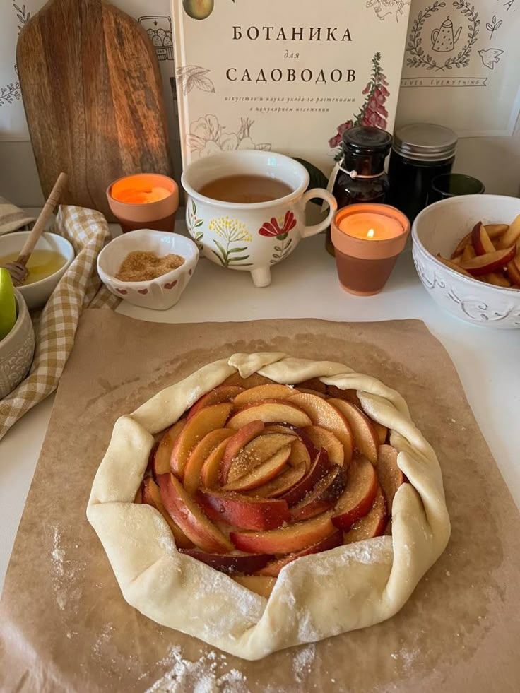 an apple pie on a table with apples and cinnamons in bowls around it, next to a book