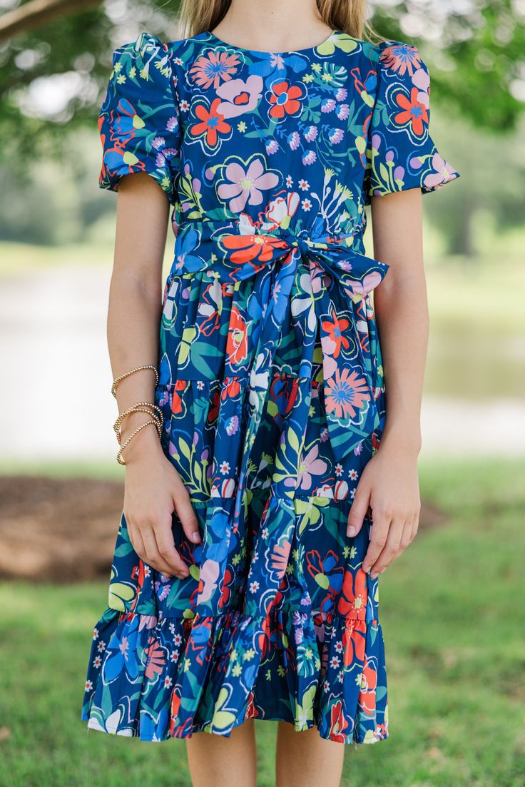 This floral dress is so bold and colorful! We just know your daughter is going to love rocking this beauty! This dress is going to be great for school, Sunday church, or any occasion where she needs to look fab! Round neckline Button keyhole back Short bubble sleeves Tied/elastic waist Floral print No stretch Morgan is wearing the small. Fun Floral Print Dress For Day Out, Fun Floral Print Dresses For Day Out, Fun Floral Print Dress For Garden Party, Fun Floral Print Dresses For Garden Party, Cute Blue Floral Summer Dress, Spring Short Sleeve School Dress, Multicolor Summer Dress For School, Cute Blue Floral Dress For Spring, Blue Spring Dress For School