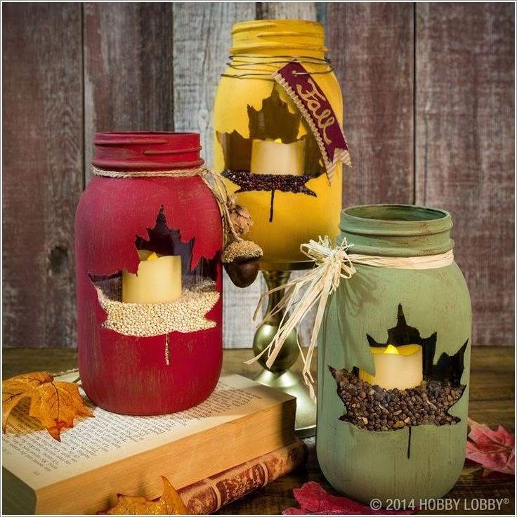 three mason jars decorated with autumn leaves and candles are sitting on top of an old book