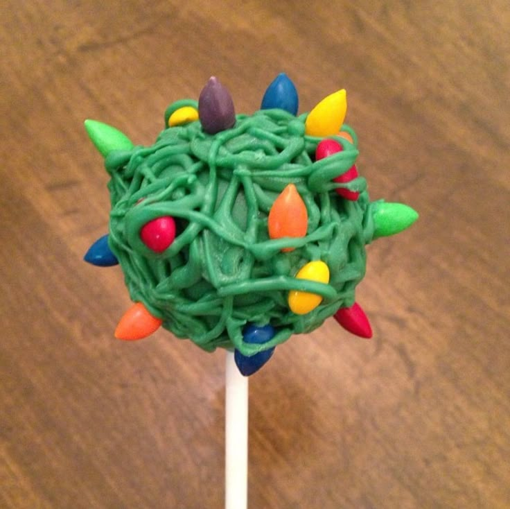 a green lollipop with christmas lights on it sitting on a wooden table next to a cupcake