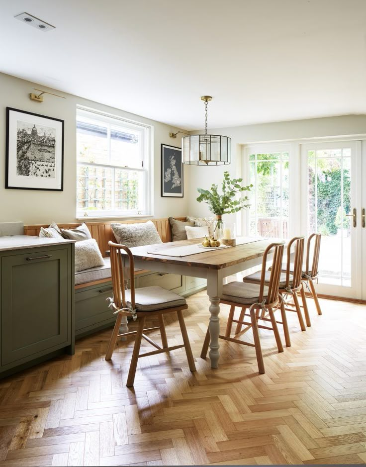 a dining room table with four chairs and a bench in front of two windows that look out onto the backyard