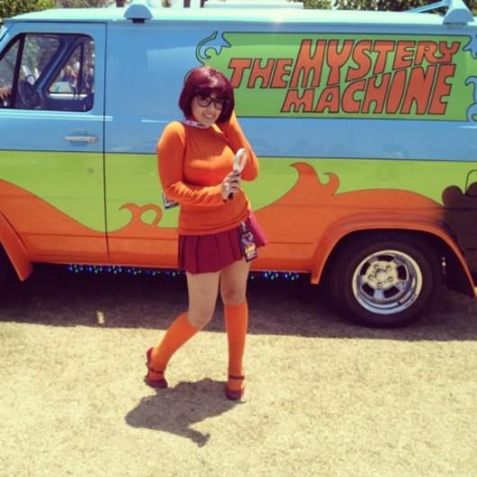 a woman standing in front of an orange and green van with the words mystery machine on it