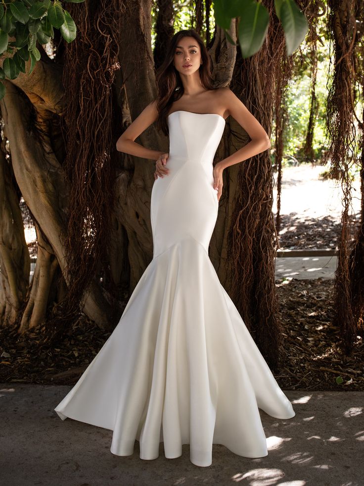 a woman standing in front of trees wearing a white wedding dress