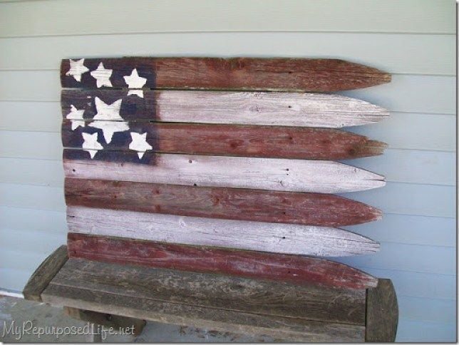 an american flag made out of wooden planks sitting on a bench in front of a house