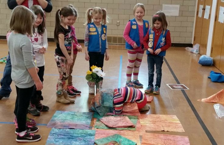 several children are standing in a room with paper on the floor and looking at something